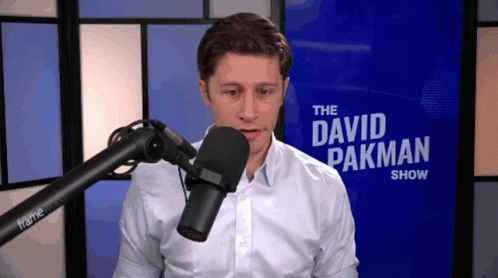 A Man Stands In Front Of A Microphone In Front Of A Sign That Says " The David Pakman Show " GIF
