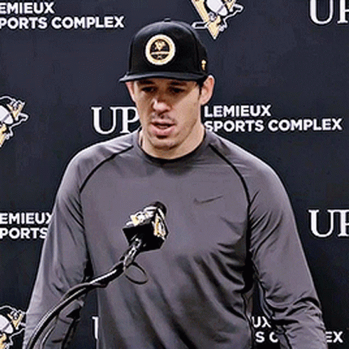 A Man Stands In Front Of A Microphone In Front Of A Wall That Says Lemieux Sports Complex GIF
