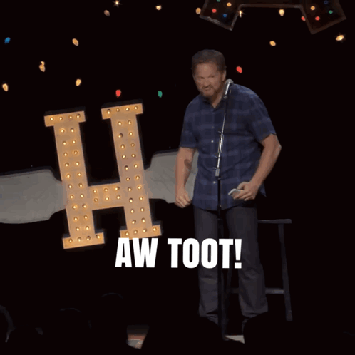 A Man Stands In Front Of A Microphone With The Words Aw Toot Behind Him GIF