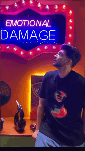 A Man Stands In Front Of A Neon Sign That Says Emotional Damage GIF