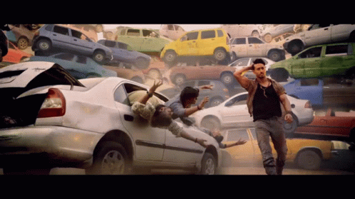 A Man Stands In Front Of A Pile Of Cars Including One That Has The Word Taxi On It GIF