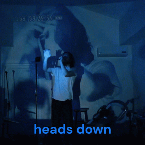 A Man Stands In Front Of A Projection Of A Woman And The Words Heads Down GIF