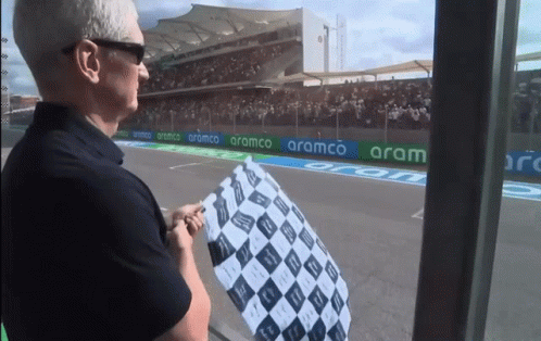A Man Stands In Front Of A Race Track With Aramco Banners GIF