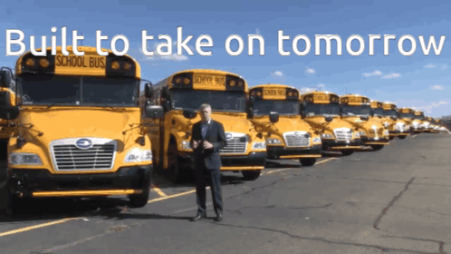 A Man Stands In Front Of A Row Of School Buses With The Words Built To Take On Tomorrow Above Him GIF