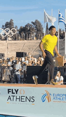 A Man Stands In Front Of A Sign That Says Fly Athens On It GIF