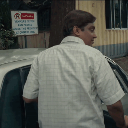 A Man Stands In Front Of A Sign That Says No Parking Vehicles Driven And Parked Inside The Premises At Owners Risk GIF