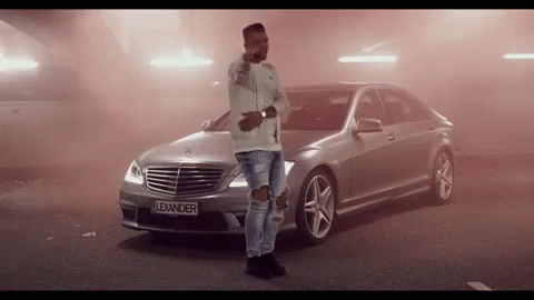 A Man Stands In Front Of A Silver Mercedes With The License Plate Lexander GIF