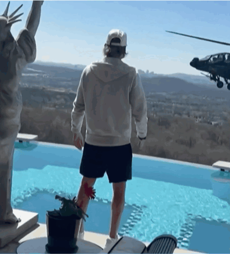 A Man Stands In Front Of A Statue Of Liberty And A Helicopter Flying Overhead GIF