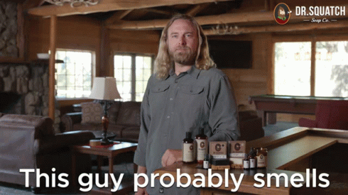 A Man Stands In Front Of A Table With Dr. Squatch Soap On It GIF