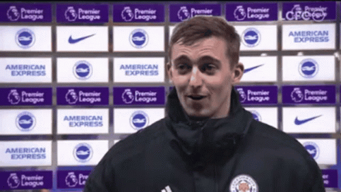 A Man Stands In Front Of A Wall Of Advertisements For American Express And Premier League GIF