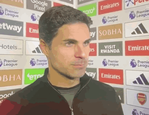 A Man Stands In Front Of A Wall Of Advertisements For Emirates GIF
