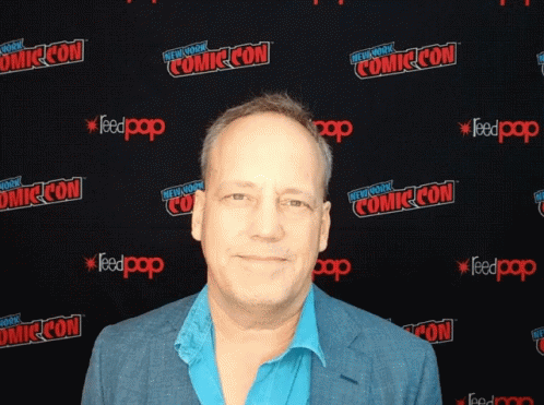 A Man Stands In Front Of A Wall That Says Comic Con On It GIF