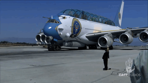 a man stands next to a large airplane that says oatestudios on the bottom
