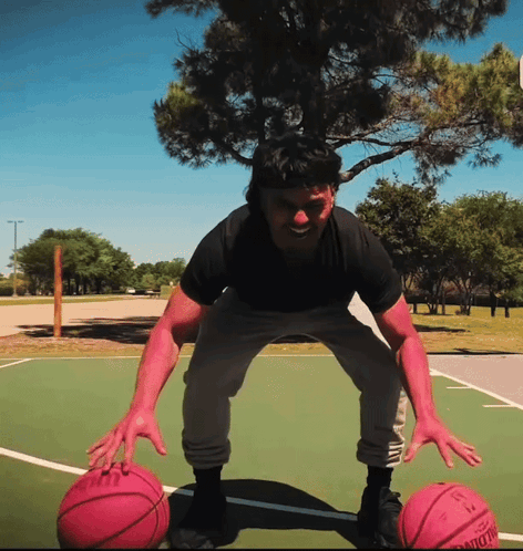 A Man Stands On A Basketball Court Holding Two Pink Basketballs One Of Which Has The Number 13 On The Back GIF