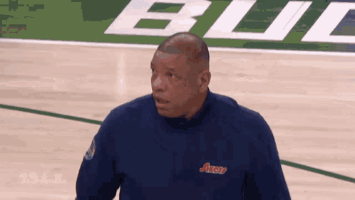 A Man Stands On A Basketball Court Wearing A Blue Shirt That Says Axerv GIF