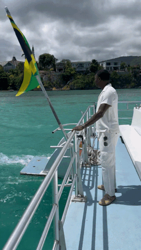 A Man Stands On A Boat With A Flag Flying In The Background GIF
