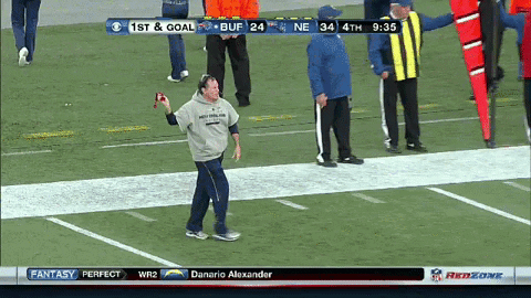 a man stands on a football field holding a ball in front of a scoreboard that says 1st and goal