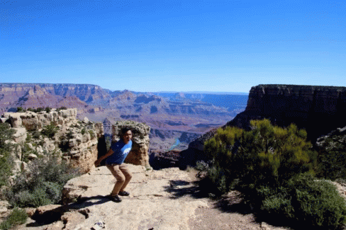 A Man Stands On A Rocky Cliff Overlooking A Canyon GIF