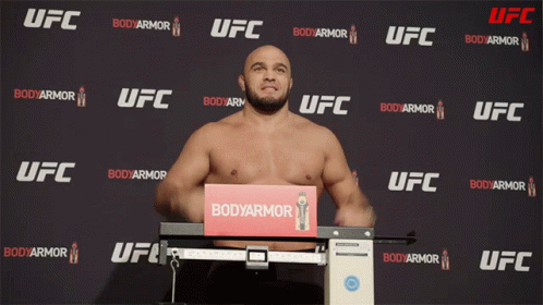 A Man Stands On A Scale In Front Of A Wall That Says Ufc GIF