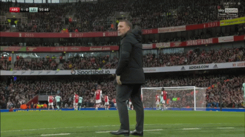 A Man Stands On A Soccer Field With Ads For Adidas.com And Arsenal.com In The Background GIF
