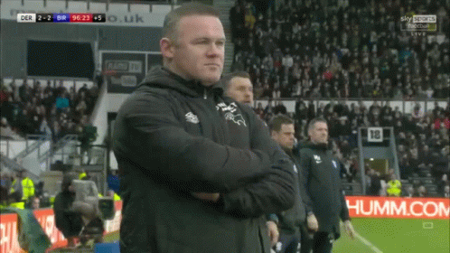 A Man Stands On A Soccer Field With His Arms Crossed In Front Of A Sky Sports Sign GIF