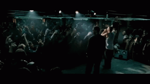 A Man Stands On A Stage In Front Of A Crowd With His Hands In The Air GIF