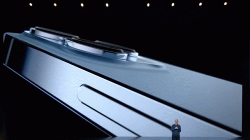 A Man Stands On A Stage In Front Of A Large Phone GIF
