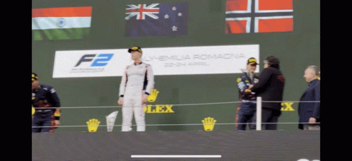 A Man Stands On A Stage In Front Of A Sign That Says F2 On It GIF
