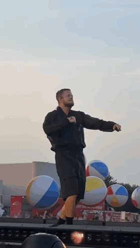 A Man Stands On A Stage In Front Of Beach Balls GIF