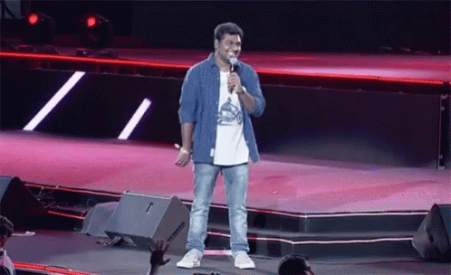 A Man Stands On A Stage With A Microphone In His Hand GIF