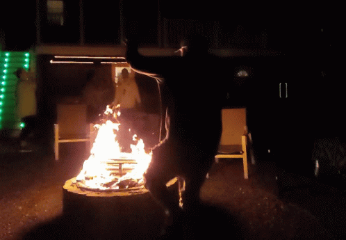 A Man Stands On A Stump In Front Of A Fire At Night GIF