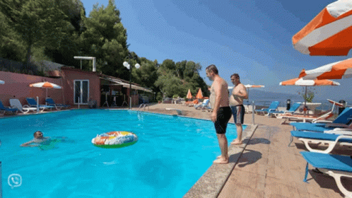 A Man Stands On The Edge Of A Swimming Pool Looking At A Float In The Water GIF