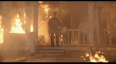 A Man Stands On The Porch Of A House That Is On Fire GIF