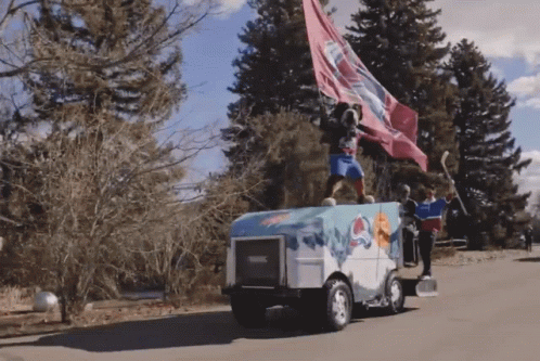 A Man Stands On Top Of An Ice Hockey Vehicle With A Flag Flying In The Wind GIF