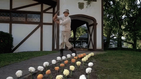 A Man Swinging A Golf Club In Front Of A Building With A Shield On It GIF