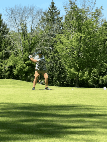 A Man Swings A Golf Club At A Golf Ball On A Golf Course GIF