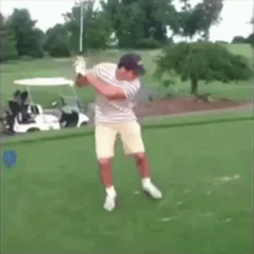 A Man Swings A Golf Club On A Golf Course In Front Of A Golf Cart GIF