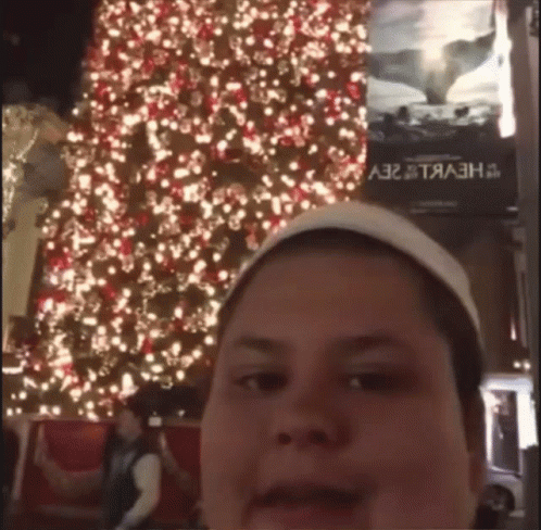 A Man Taking A Picture In Front Of A Christmas Tree GIF