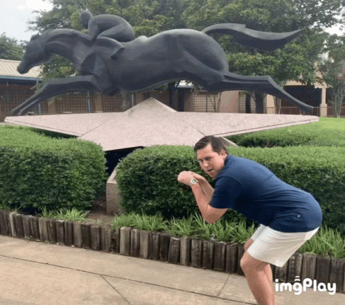 A Man Taking A Picture Of A Statue Of A Horse And Jockey With Imgplay Written Below Him GIF
