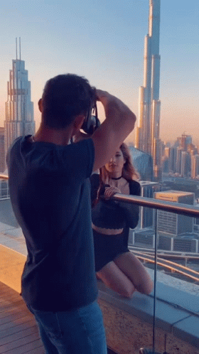 A Man Taking A Picture Of A Woman Sitting On A Balcony GIF