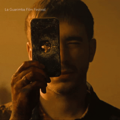 A Man Taking A Picture Of Himself With A La Guarimba Film Festival Advertisement In The Background GIF