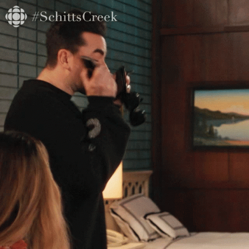 A Man Taking A Picture With A Camera With #Schitts Creek On The Bottom GIF