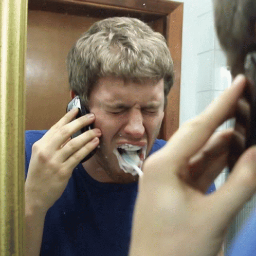A Man Talking On A Cell Phone While Brushing His Teeth In Front Of A Mirror GIF