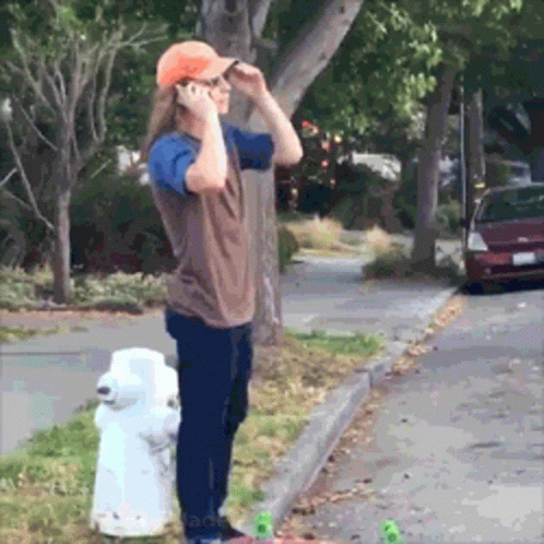 A Man Talking On A Cell Phone While Standing Next To A White Fire Hydrant GIF