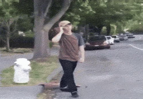 A Man Talking On A Cell Phone While Walking Down A Street GIF