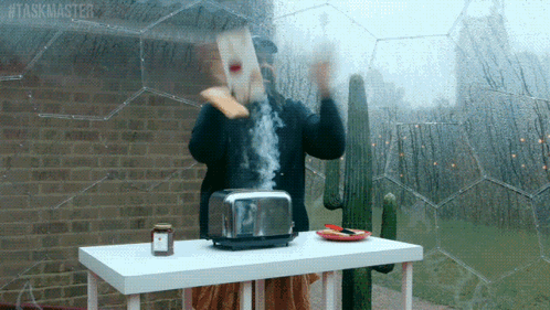 A Man Throws A Piece Of Toast Into A Toaster With The Hashtag # Taskmaster GIF