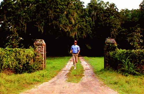 A Man Walking Down A Dirt Road In A Field GIF