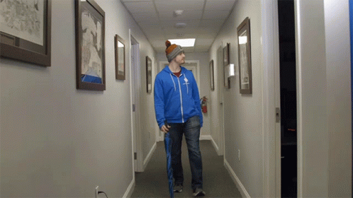 A Man Walking Down A Hallway With A Blue Jacket That Says ' Abercrombie & Fitch ' On The Front GIF