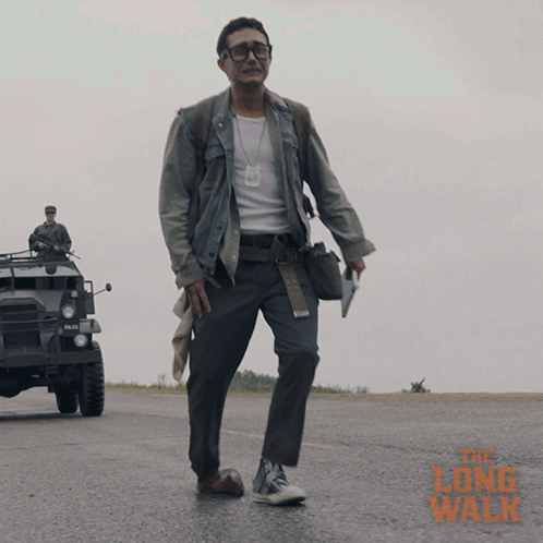A Man Walking Down A Road With The Long Walk Written In Orange GIF