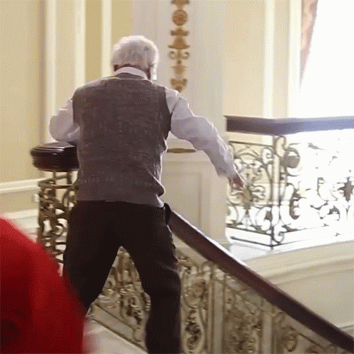 A Man Walking Down A Set Of Stairs With A Wrought Iron Railing Behind Him GIF